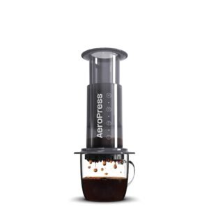 AeroPress coffee maker on white background, brewing into a glass mug
